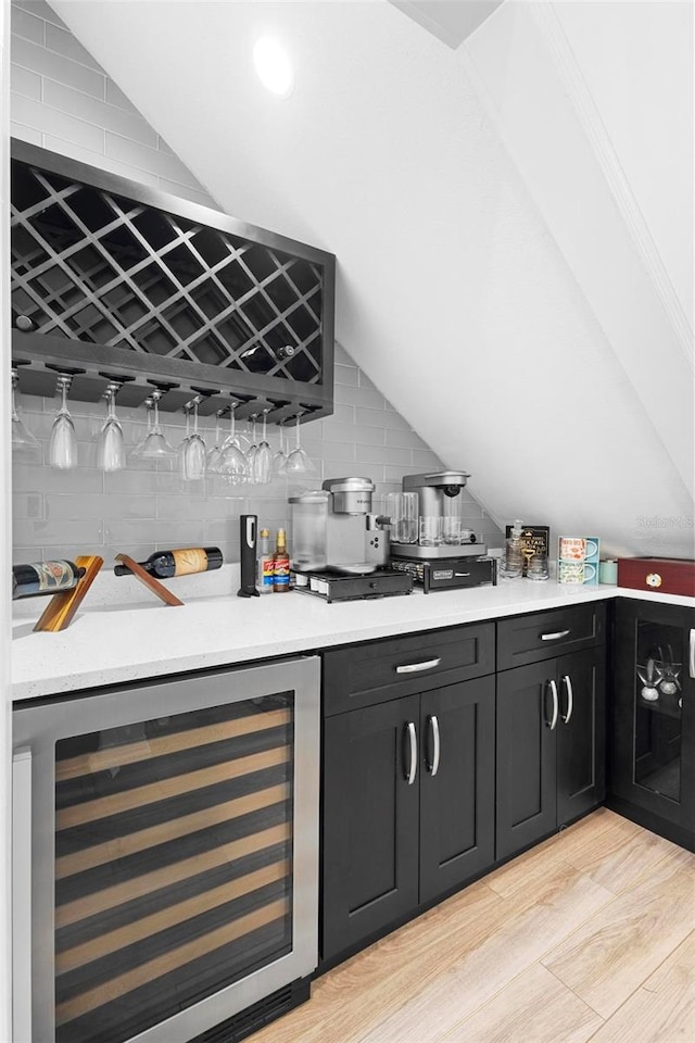 bar featuring light wood-type flooring, lofted ceiling, beverage cooler, and tasteful backsplash