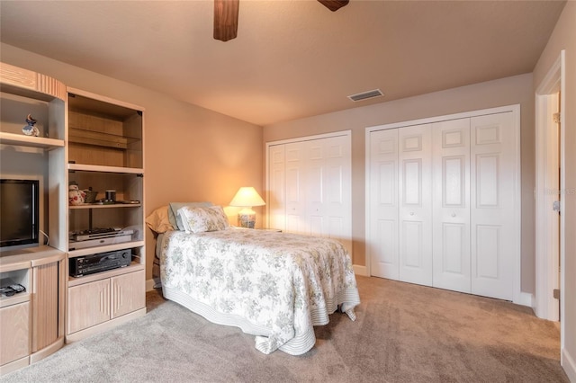 bedroom featuring ceiling fan, light carpet, and two closets