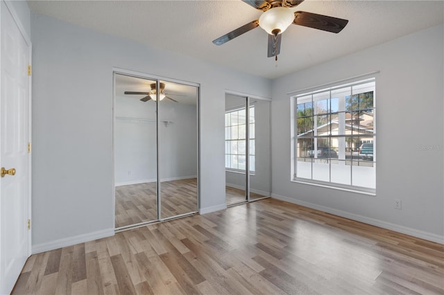 unfurnished bedroom featuring two closets, ceiling fan, light hardwood / wood-style floors, and a textured ceiling