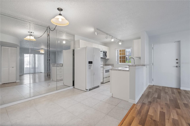 kitchen with white appliances, hanging light fixtures, kitchen peninsula, a textured ceiling, and white cabinets