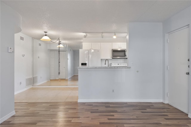 kitchen featuring hardwood / wood-style floors, white fridge with ice dispenser, kitchen peninsula, a textured ceiling, and white cabinetry