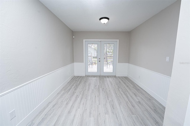 interior space with a wainscoted wall, wood finished floors, and french doors