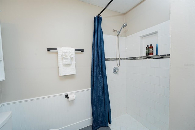 full bath featuring wainscoting, a tile shower, and toilet