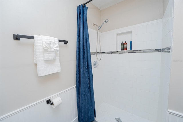 bathroom with a wainscoted wall and a tile shower