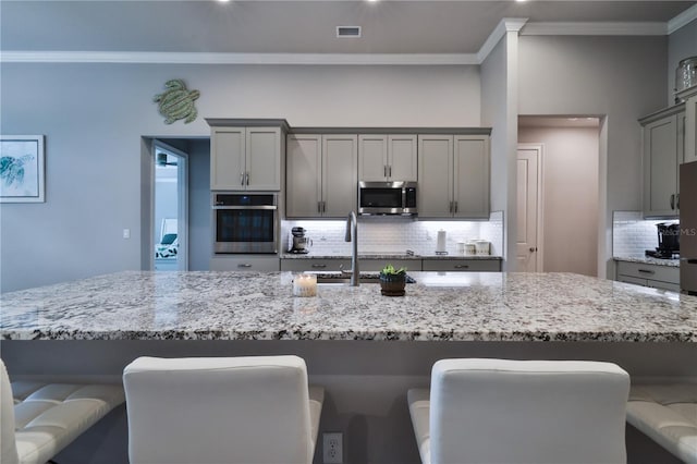 kitchen with gray cabinetry, sink, appliances with stainless steel finishes, tasteful backsplash, and a breakfast bar area