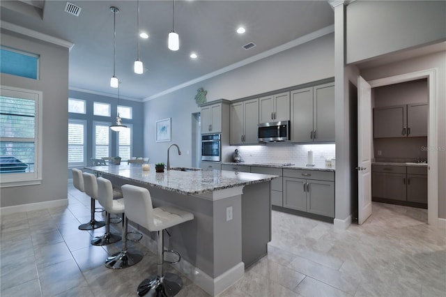 kitchen with light stone countertops, appliances with stainless steel finishes, a kitchen island with sink, and gray cabinetry