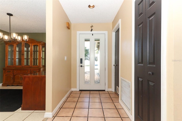 entryway with a chandelier, light tile patterned flooring, visible vents, and a textured ceiling