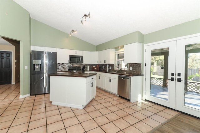 kitchen featuring white cabinets, decorative backsplash, dark countertops, appliances with stainless steel finishes, and vaulted ceiling