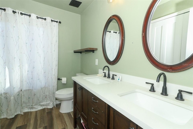 bathroom featuring double vanity, a sink, toilet, and wood finished floors