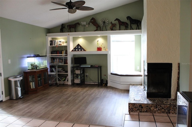 living room with a fireplace with raised hearth, wood finished floors, lofted ceiling, and a ceiling fan