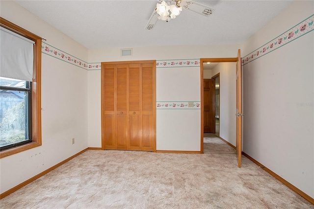 unfurnished bedroom featuring ceiling fan, light colored carpet, a textured ceiling, and a closet