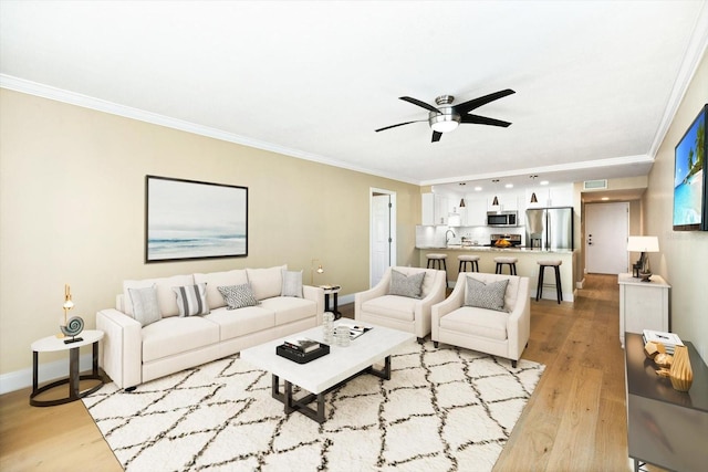 living room with ceiling fan, light wood-type flooring, sink, and crown molding