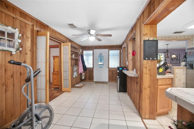 kitchen with wooden walls, tile countertops, ceiling fan, light tile patterned floors, and hanging light fixtures