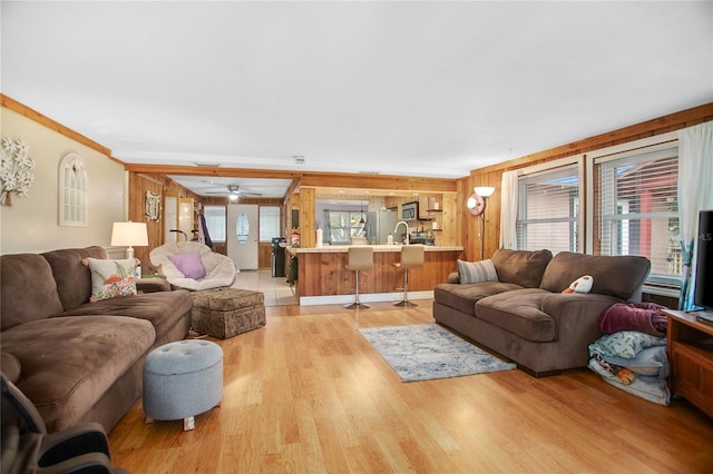 living room featuring light hardwood / wood-style flooring, wood walls, crown molding, ceiling fan, and sink