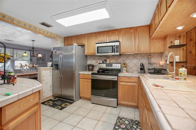 kitchen featuring tile countertops, a notable chandelier, light tile patterned floors, backsplash, and appliances with stainless steel finishes