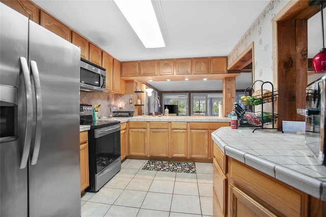 kitchen with stainless steel appliances, tile countertops, decorative backsplash, sink, and light tile patterned flooring