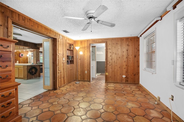 spare room featuring a textured ceiling, wood walls, ceiling fan, and crown molding