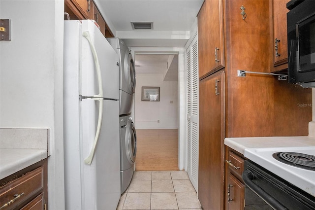 kitchen with light tile patterned flooring, stacked washer and clothes dryer, and white refrigerator