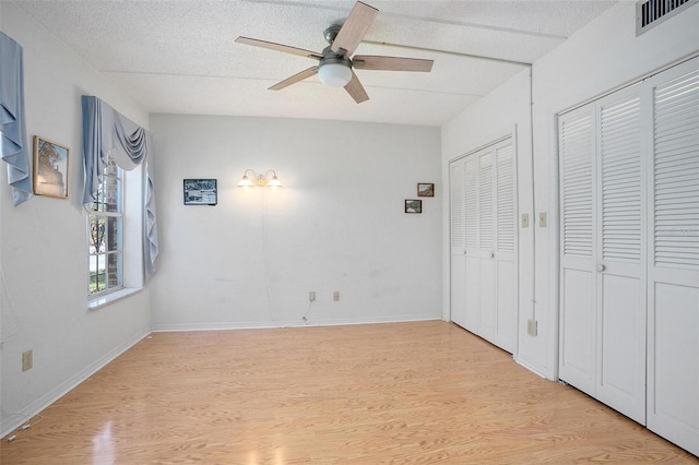 unfurnished bedroom with ceiling fan, two closets, light hardwood / wood-style floors, and a textured ceiling