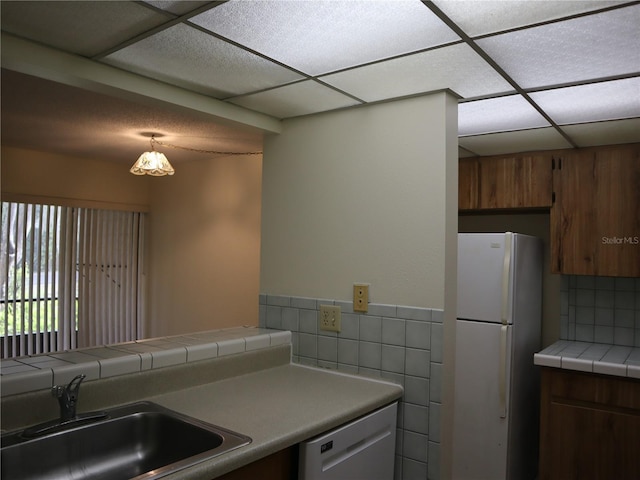 kitchen featuring tile counters, decorative backsplash, dishwasher, white refrigerator, and sink