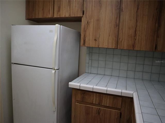 kitchen featuring tile countertops, decorative backsplash, and white refrigerator