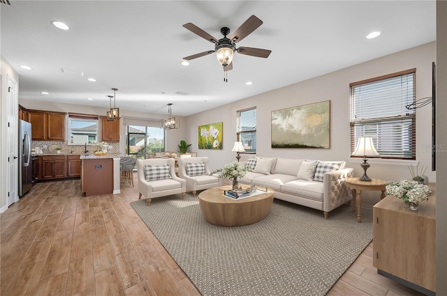 living room with ceiling fan with notable chandelier and light hardwood / wood-style flooring