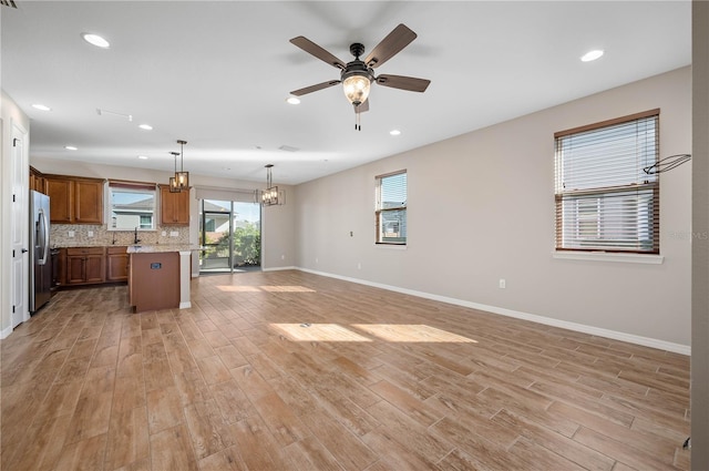 kitchen with ceiling fan with notable chandelier, pendant lighting, a kitchen island, stainless steel fridge, and light hardwood / wood-style flooring