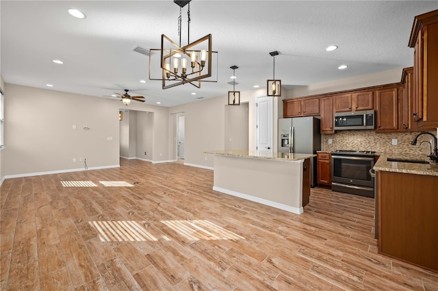 kitchen featuring a kitchen island, sink, hanging light fixtures, appliances with stainless steel finishes, and ceiling fan with notable chandelier