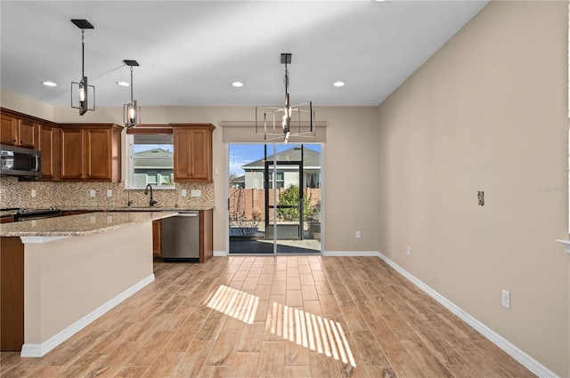 kitchen with decorative light fixtures, sink, light stone counters, and stainless steel appliances