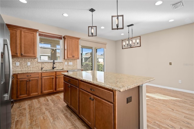 kitchen featuring pendant lighting, a kitchen island, sink, an inviting chandelier, and stainless steel fridge