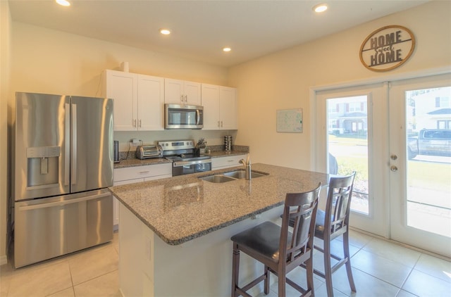 kitchen with white cabinets, french doors, stainless steel appliances, and a center island with sink