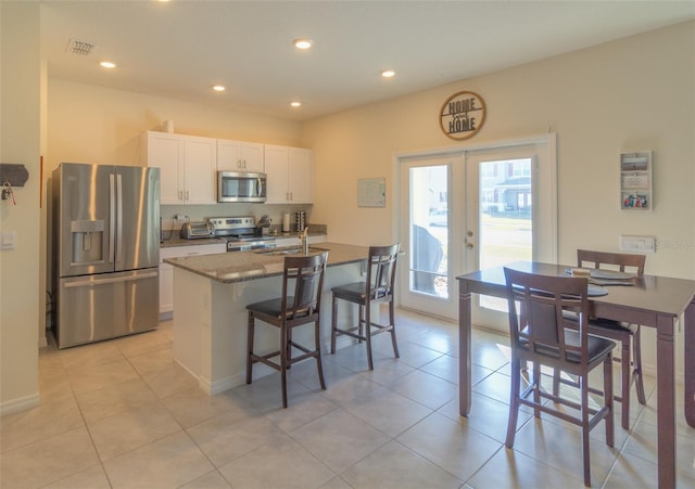 kitchen with french doors, a center island with sink, white cabinets, appliances with stainless steel finishes, and a breakfast bar area