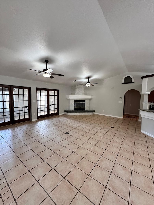 unfurnished living room with french doors, a textured ceiling, vaulted ceiling, ceiling fan, and light tile patterned floors