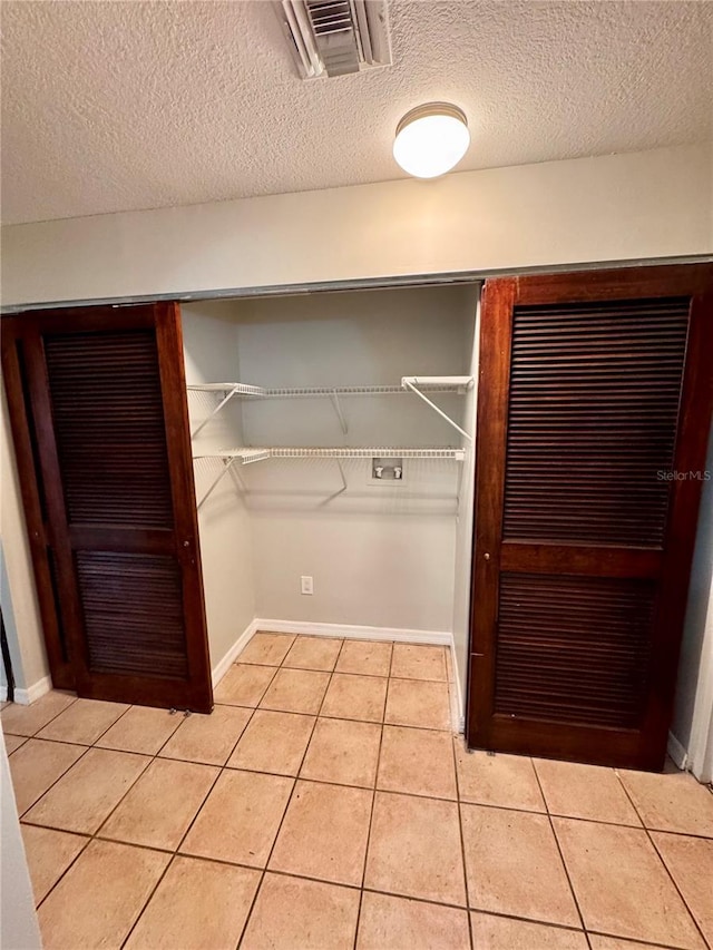 interior space with light tile patterned floors, a textured ceiling, and hookup for a washing machine