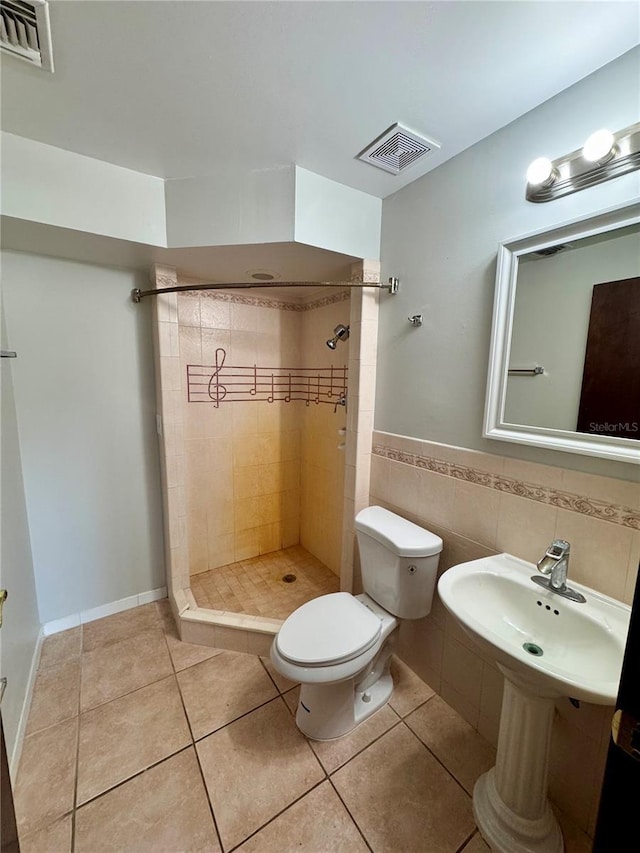 bathroom featuring tile patterned floors, toilet, tiled shower, and tile walls