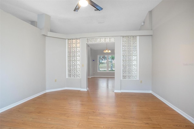 unfurnished room featuring ceiling fan with notable chandelier and light hardwood / wood-style flooring