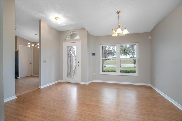 foyer entrance with a textured ceiling, light wood-type flooring, lofted ceiling, and a chandelier