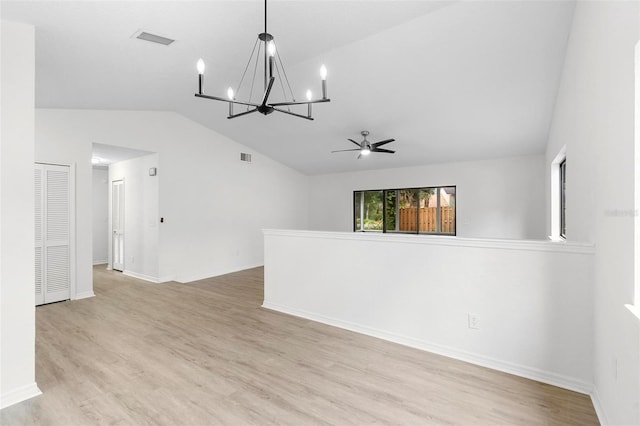 empty room with ceiling fan with notable chandelier, light wood-type flooring, and vaulted ceiling