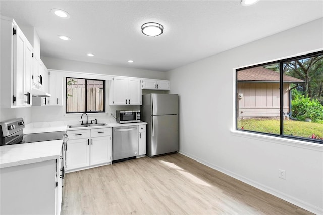 kitchen with light stone counters, light hardwood / wood-style floors, white cabinets, appliances with stainless steel finishes, and sink