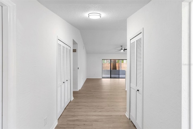 corridor featuring lofted ceiling, a textured ceiling, and light hardwood / wood-style floors