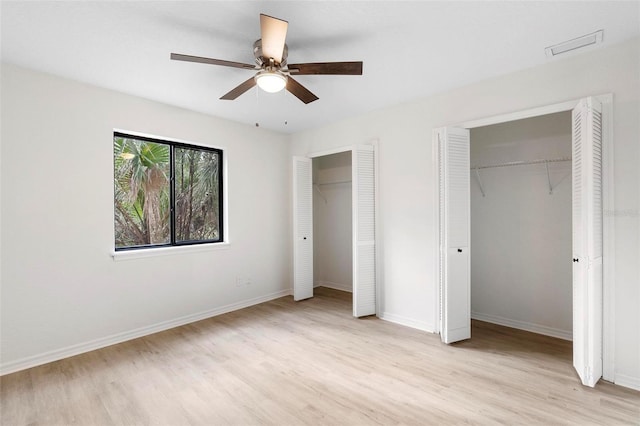 unfurnished bedroom featuring light wood-type flooring, ceiling fan, and multiple closets