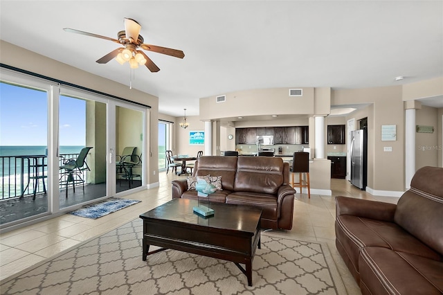 tiled living room featuring a water view, a wealth of natural light, and ceiling fan with notable chandelier