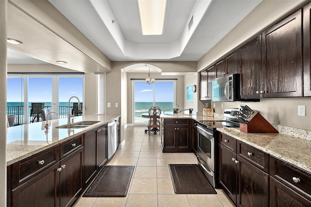 kitchen with appliances with stainless steel finishes, sink, a raised ceiling, a water view, and light stone counters