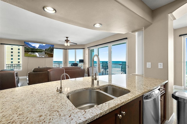 kitchen featuring stainless steel dishwasher, ceiling fan, light stone countertops, and sink