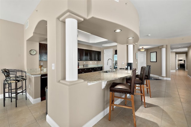 kitchen featuring a kitchen breakfast bar, light stone countertops, sink, and light tile patterned flooring