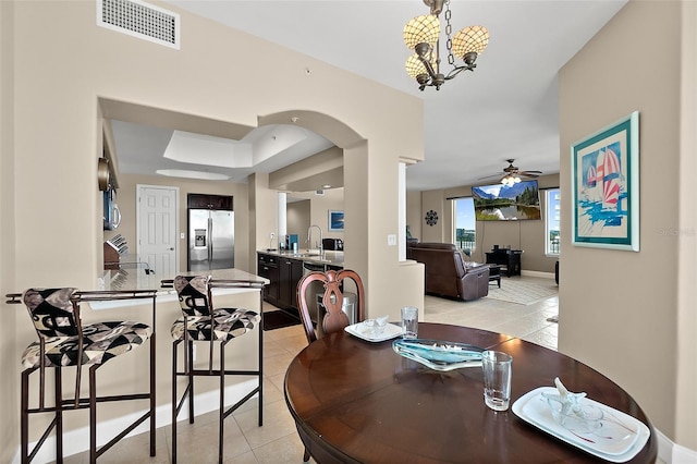 tiled dining area featuring a tray ceiling, sink, and ceiling fan with notable chandelier