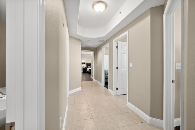 hall featuring a raised ceiling and light tile patterned floors