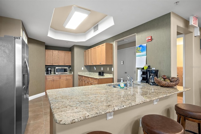 kitchen with a raised ceiling, appliances with stainless steel finishes, sink, and a kitchen breakfast bar