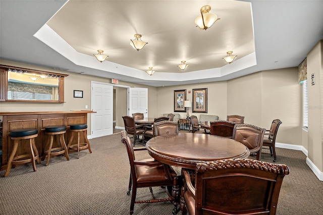 carpeted dining room featuring indoor bar and a raised ceiling