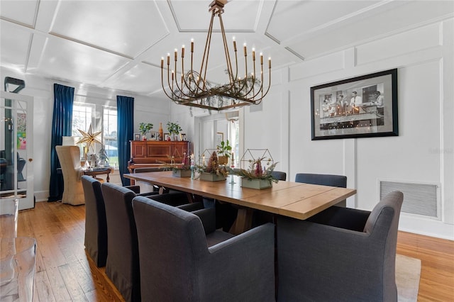 dining space with coffered ceiling, an inviting chandelier, and light hardwood / wood-style floors